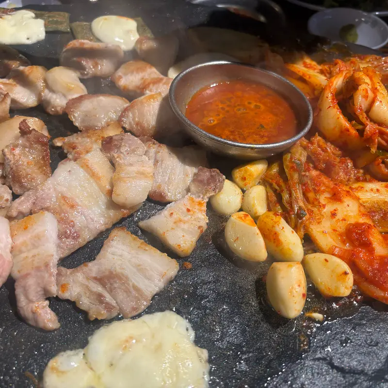 돌판 위에 고기, 김치, 마늘, 젓갈이 함께 구워지고 있는 모습
