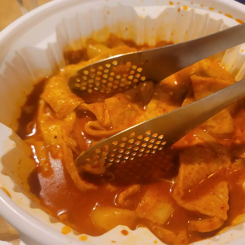 엽기떡볶이 속 떡과 어묵을 집게로 들어올린 모습