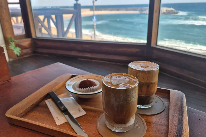 바다를 배경으로 놓인 두 잔의 커피와 디저트