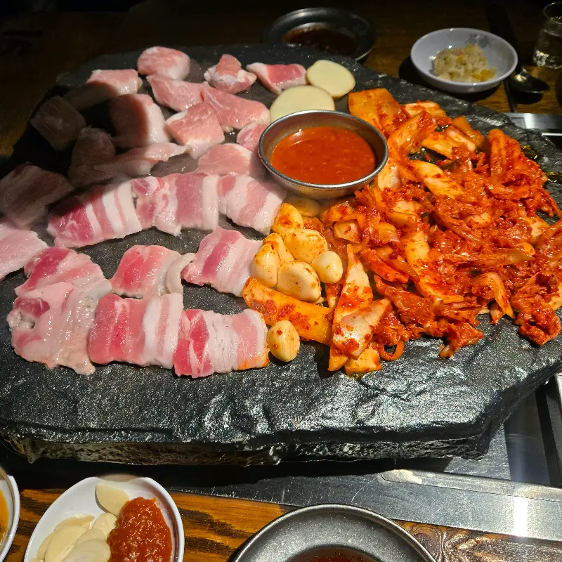 돌판 위에 삼겹살, 김치, 젓갈이 함께 구워지고 있는 모습