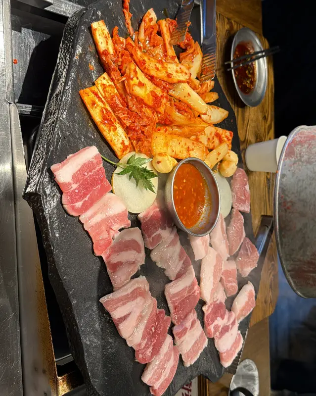 돌판 위에 삼겹살, 김치, 마늘이 함께 구워지는 모습