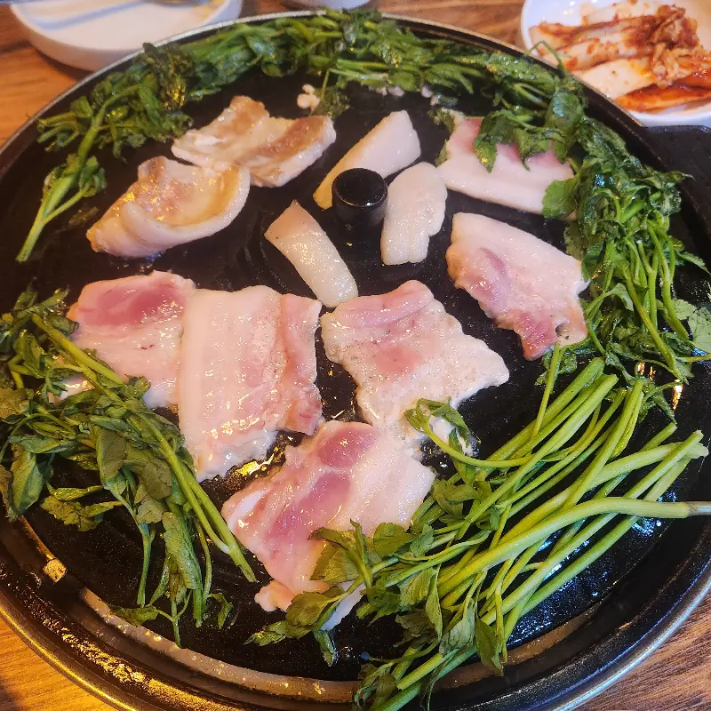 솥뚜껑 가득 구워진 삼겹살과 미나리