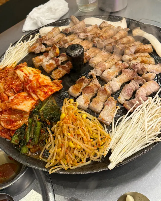 솥뚜껑 가득 올려진 삼겹살과 곁들임 채소