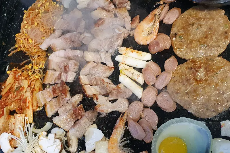 불판 위에서 익어가는 삼겹살과 다양한 재료들