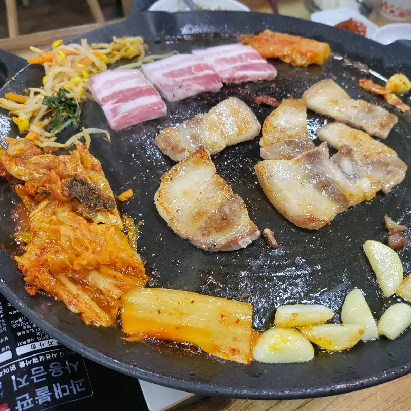 불판 위에서 구워지는 삼겹살, 김치, 마늘