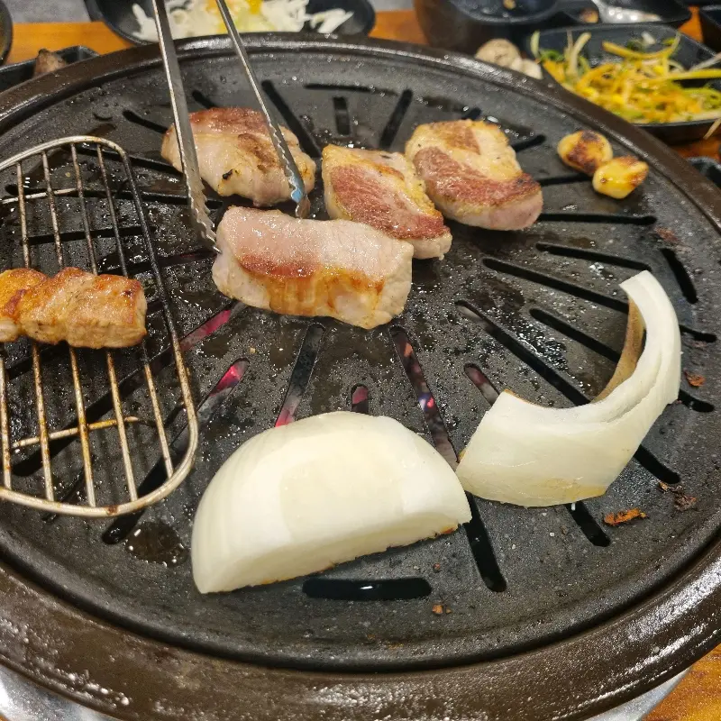 잘 구워진 오겹살 옆으로 양파와 마늘이 함께 구워지고 있는 모습이 보인다.