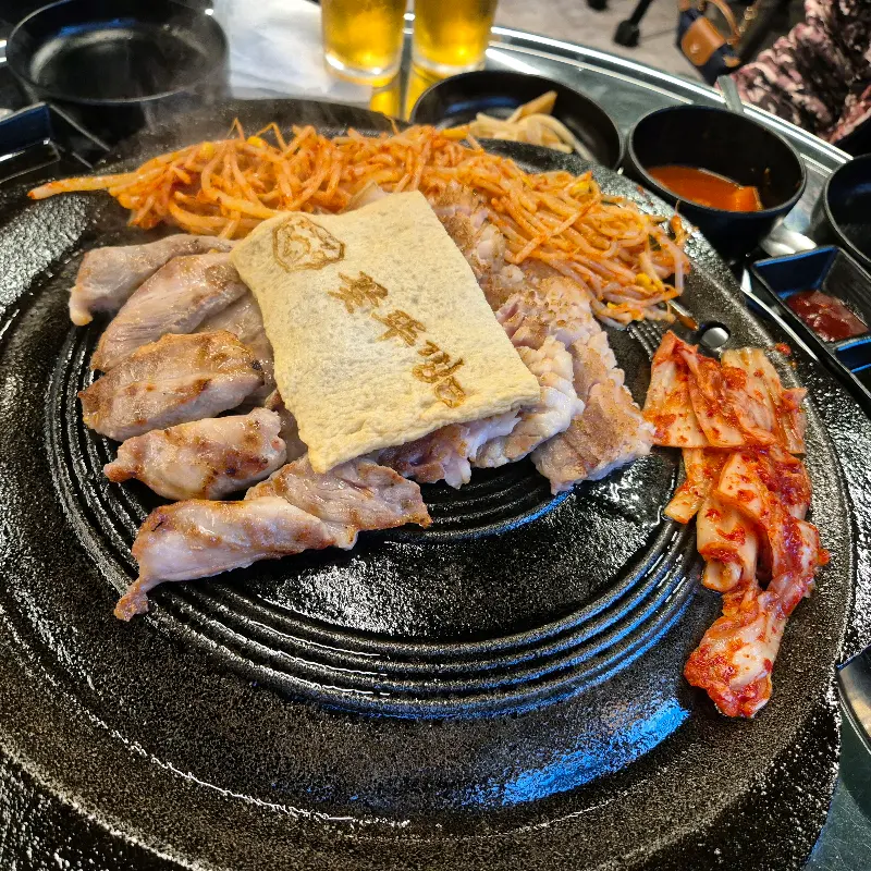 솥뚜껑에 삼겹살, 김치, 콩나물, 그리고 꽃뚜껑 도장이 찍힌 두부