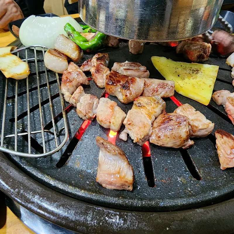 불판 위에서 노릇하게 구워지고 있는 오겹살 조각들의 모습이 클로즈업 되어 있다.