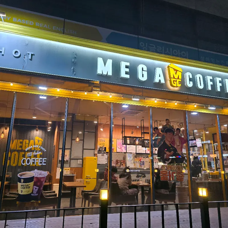 밤에 찍은 메가커피 외부 사진. 노란색 간판이 멀리서도 눈에 띈다.