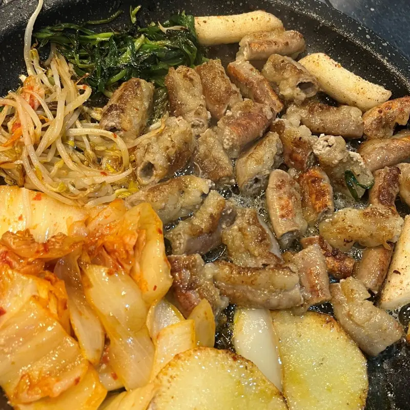 노릇하게 구워진 곱창과 김치, 떡, 부추가 조화롭게 담긴 불판 사진