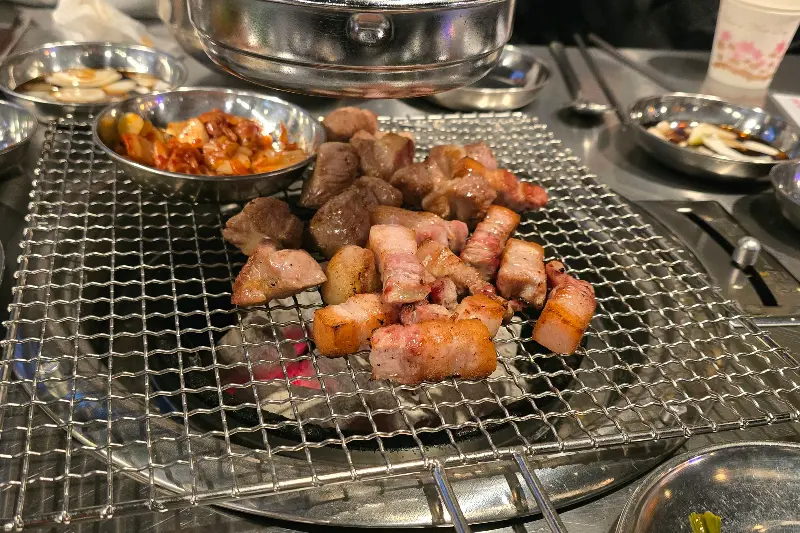 불판 위에 올려진 삼겹살, 김치, 마늘