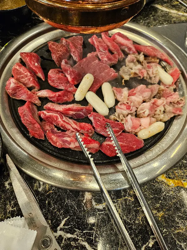 불판 위에서 익어가는 고기, 라면 사리, 떡