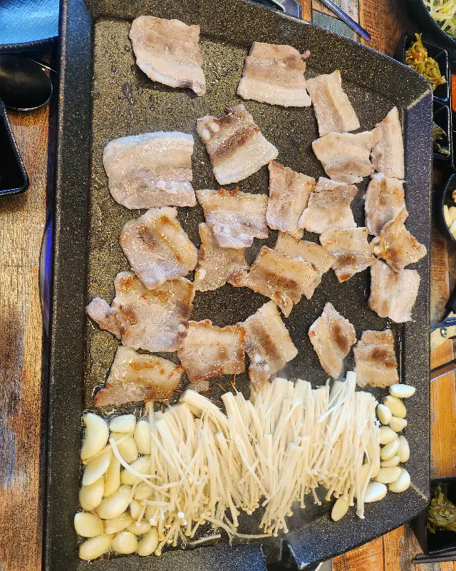 불판 위에 구워진 삼겹살과 김치, 마늘