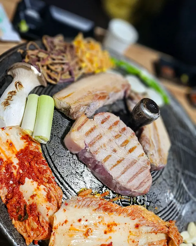 솥뚜껑 위에 삼겹살, 김치, 콩나물, 고사리를 함께 구워 먹는 모습