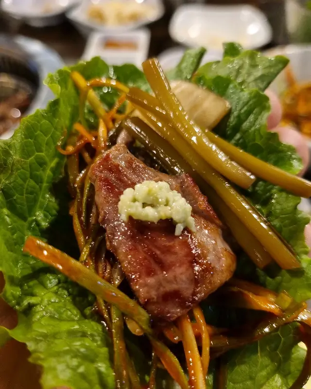 잘 구워진 고기를 깻잎, 파김치 등과 함께 싸 먹는 모습