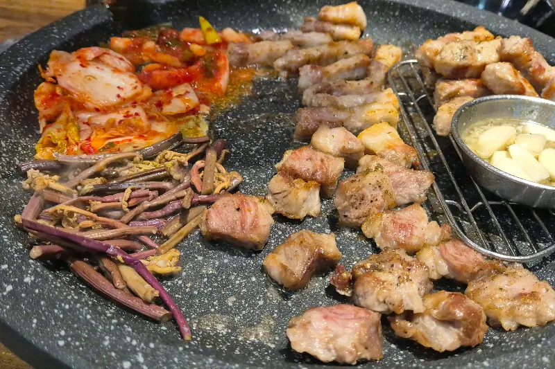 불판 위에 가지런히 놓인 삼겹살과 김치, 고사리의 조화