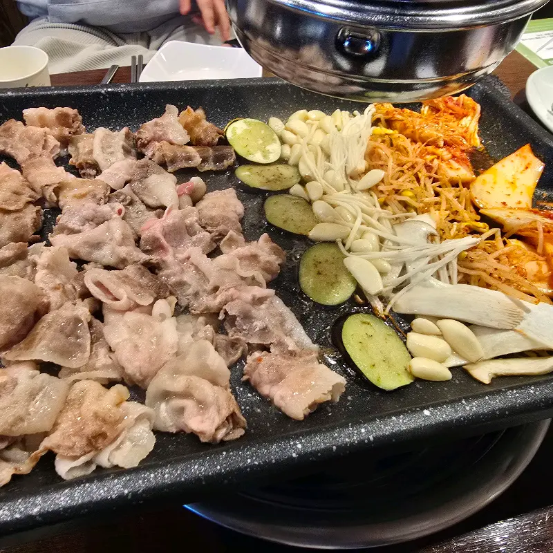 불판 가득 구워진 대패 삼겹살, 김치, 콩나물, 마늘