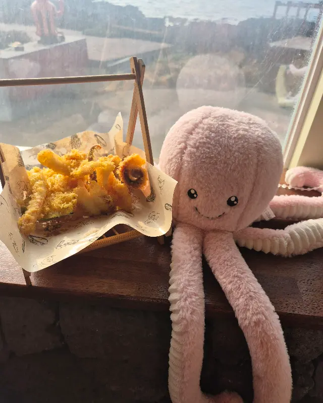 창가 자리에 앉아 바다를 바라보며 식사를 즐기는 모습. 앙증맞은 문어 인형이 시선을 사로잡는다.