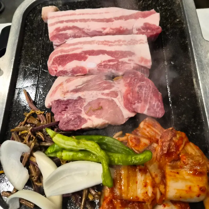 불판 위에 삼겹살과 함께 구워지고 있는 김치와 고사리의 모습