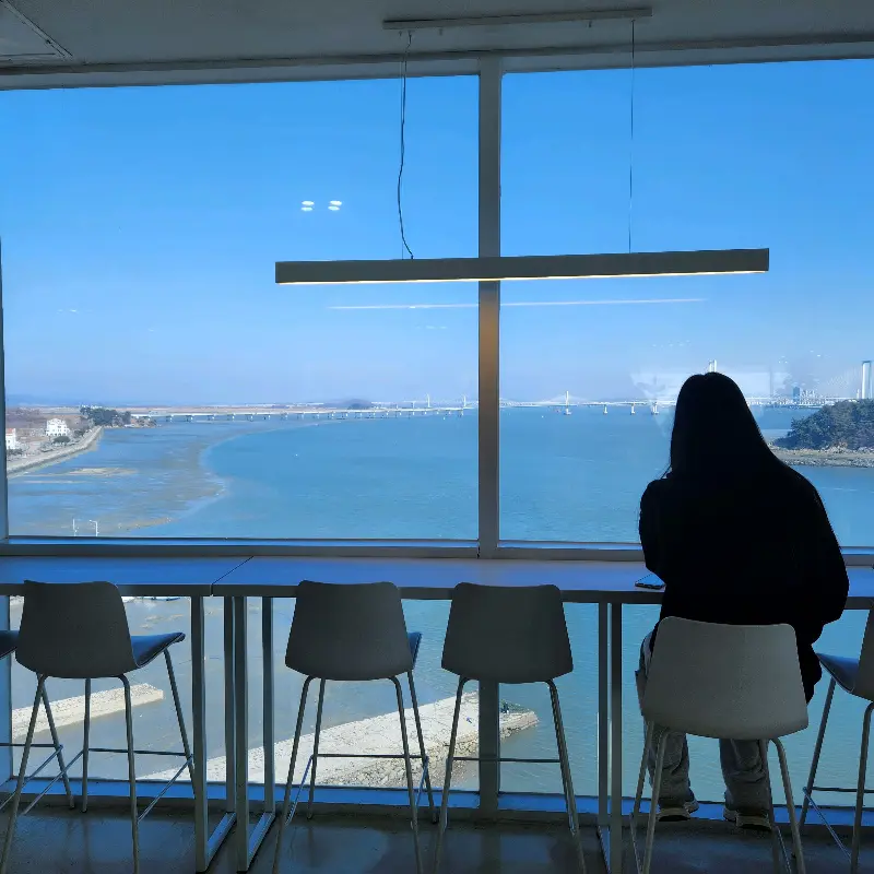 통창 앞에 앉아 바다를 바라보는 사람들의 모습