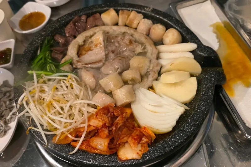 잘 구워진 곱창, 대창, 막창, 염통, 김치, 떡, 양파가 불판 위에 놓여있는 모습