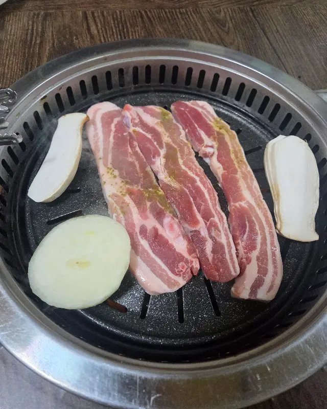 불판 위에서 익어가는 삼겹살과 버섯, 양파
