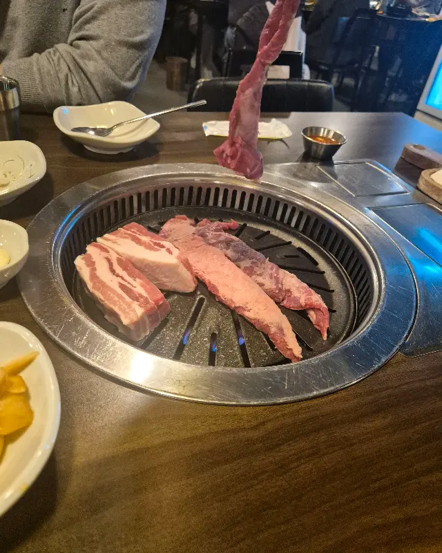 삼겹살, 목살, 갈매기살이 불판 위에 올려져 있는 모습