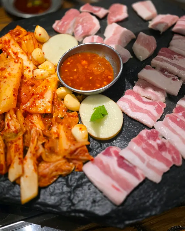 김치, 마늘, 삼겹살이 돌판에서 조화롭게 구워진 모습