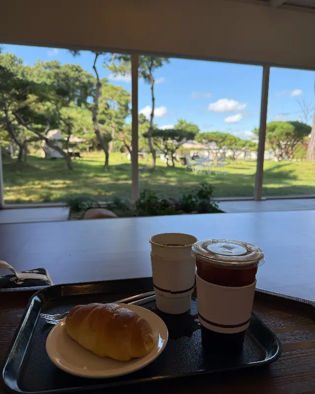 테이블에 놓인 커피와 빵, 그리고 창밖으로 보이는 푸른 정원