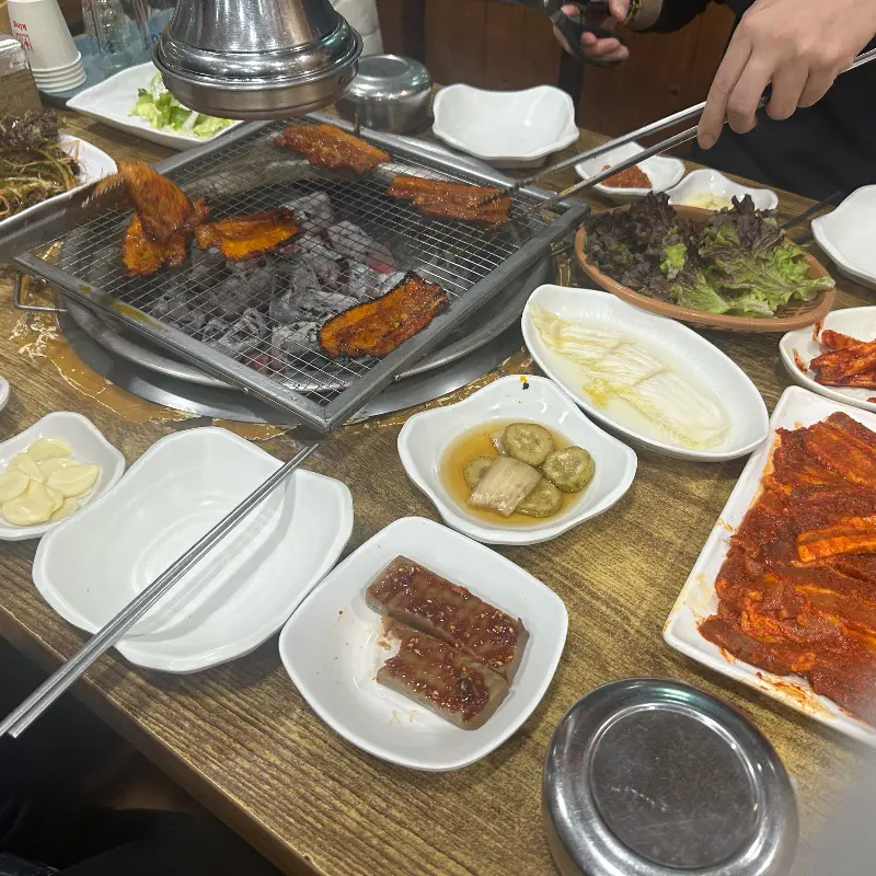 숯불 위에 올려진 고추장 화로구이와 다양한 밑반찬