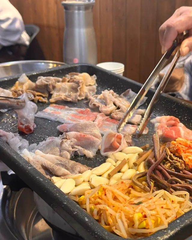 불판 위에 푸짐하게 올려진 대패 삼겹살과 곁들임 채소