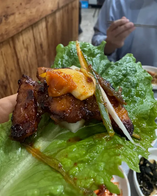 싱싱한 상추에 양념 삼겹살, 파채, 쌈무를 올려 한 입 가득