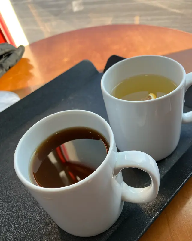 따뜻한 커피와 차가 담긴 머그컵. 햇살이 은은하게 비추는 모습이 따뜻하다.