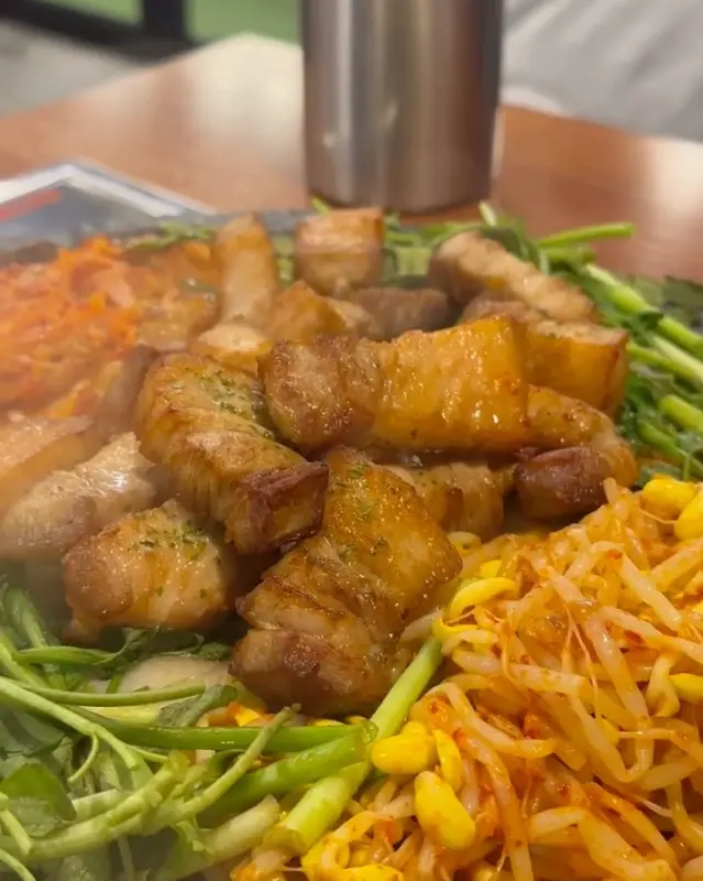 돌판 위에 놓인 삼겹살과 안심, 미나리, 콩나물, 김치의 조화로운 모습