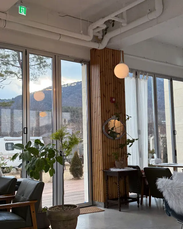 통창으로 보이는 푸른 나무와 산이 아름다운 카페 내부