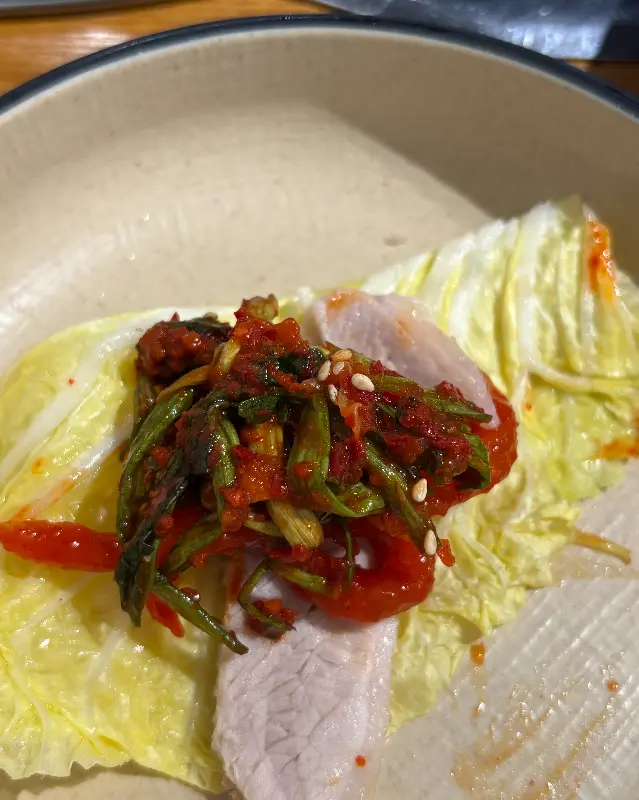 배추에 보쌈과 미나리김치를 함께 싸서 먹는 모습