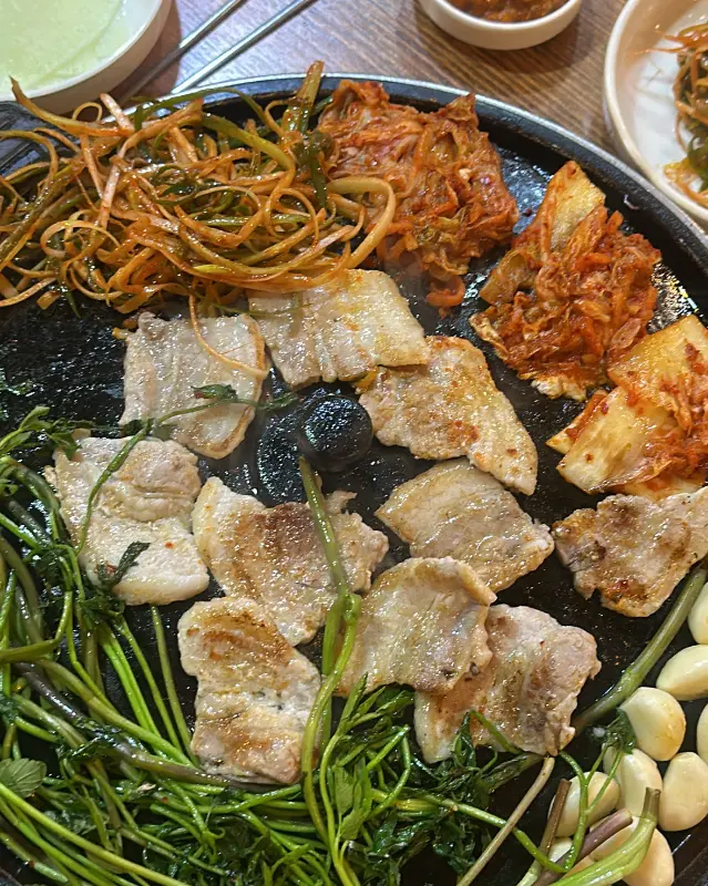 솥뚜껑에 구워지는 삼겹살과 김치, 콩나물