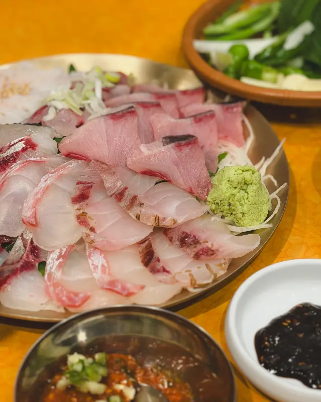 신선한 회 한 상 차림: 다양한 종류의 회와 곁들임 찬들이 정갈하게 담겨 있으며, 특히 회의 윤기가 신선함을 강조한다.