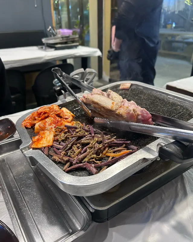 불판 위에서 익어가는 삼겹살, 김치, 고사리의 모습