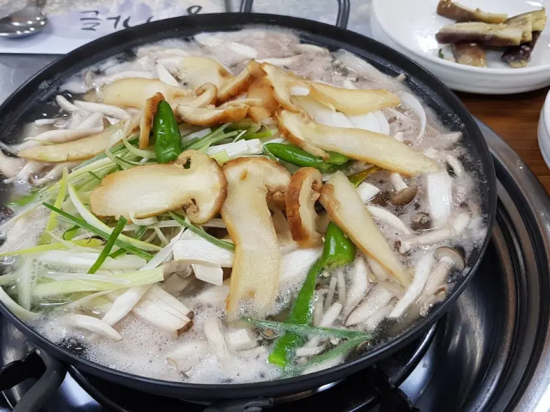 테이블 위 버섯 전골 냄비의 클로즈업 샷입니다. 전골에는 여러 종류의 버섯과 채소가 들어 있습니다.