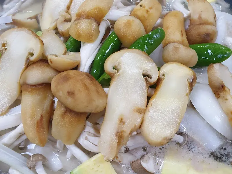 얇게 썬 다양한 종류의 버섯과 녹색 채소가 담긴 냄비 클로즈업.