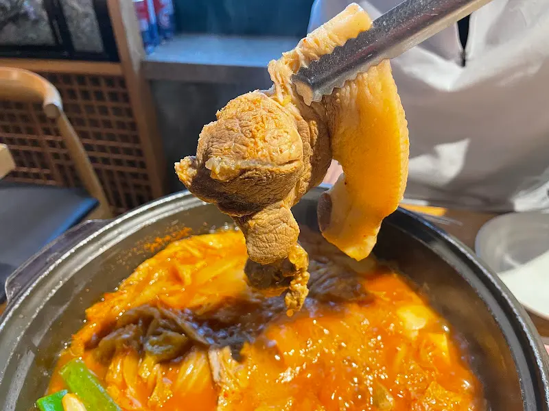 김치와 돼지고기를 집게로 들어 올리는 모습이 먹음직스럽다.