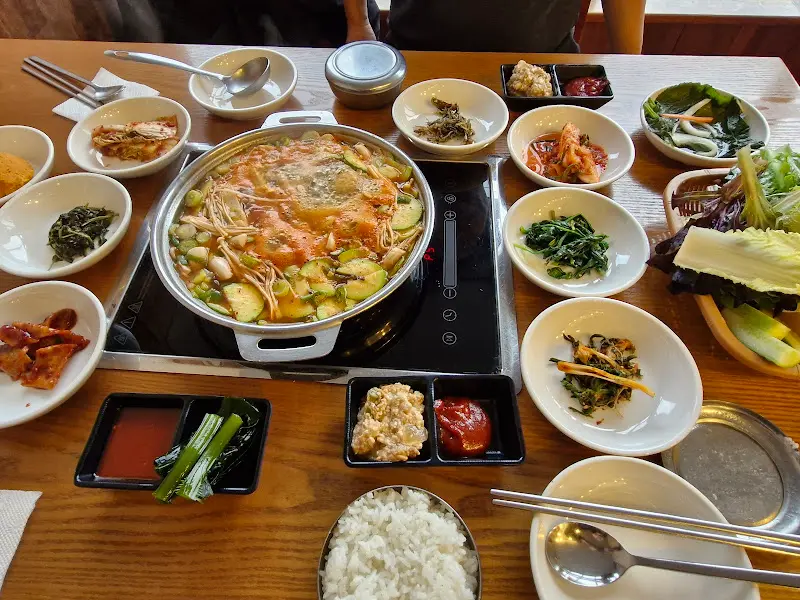 두부전골이 가운데 놓여있고, 쌈 채소와 다양한 반찬들이 테이블을 가득 채운 모습