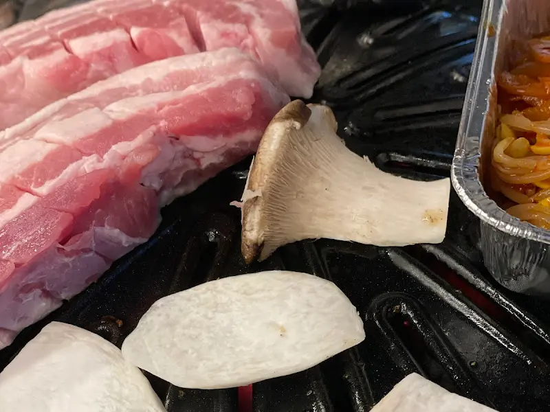 불판 위에 삼겹살, 큼지막한 새송이버섯, 양파가 함께 구워지고 있다.