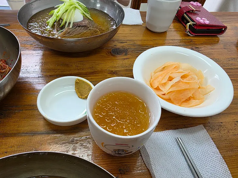 테이블 위에 놓인 물냉면, 비빔냉면 사리, 컵, 냅킨, 수저