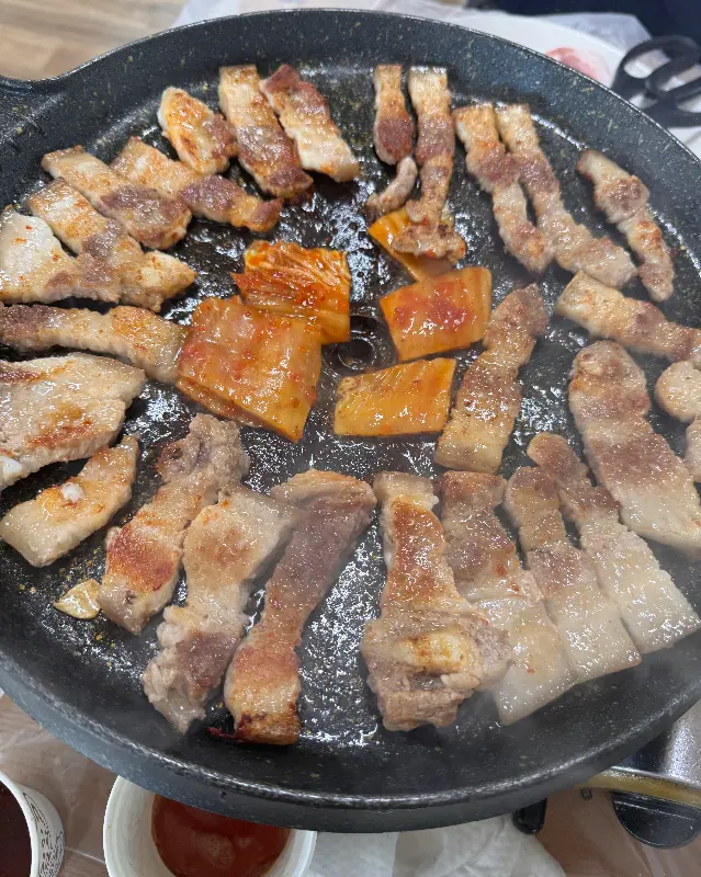 불판 위에서 익어가는 흑돼지 삼겹살과 김치