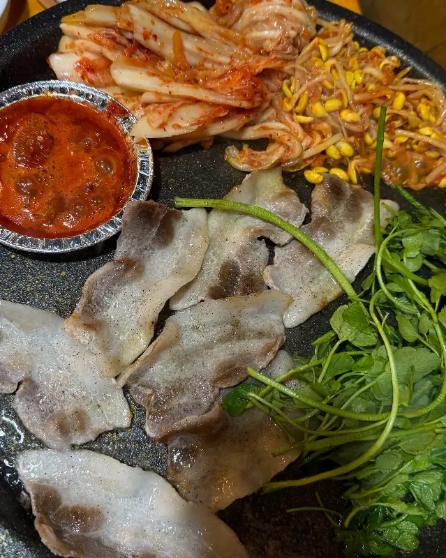 불판 위 삼겹살과 김치, 콩나물, 미나리