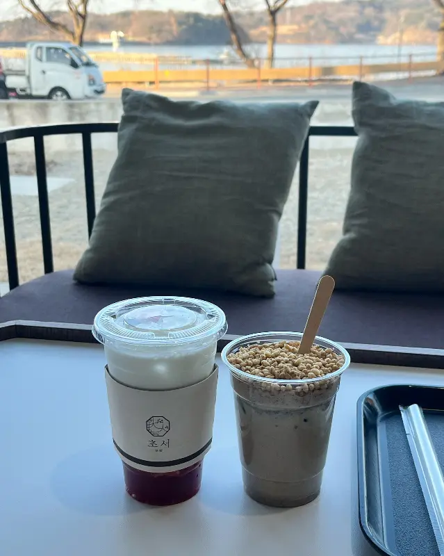 창밖의 탑정호 풍경을 배경으로 놓인 흑임자 크림 라떼와 딸기 라떼