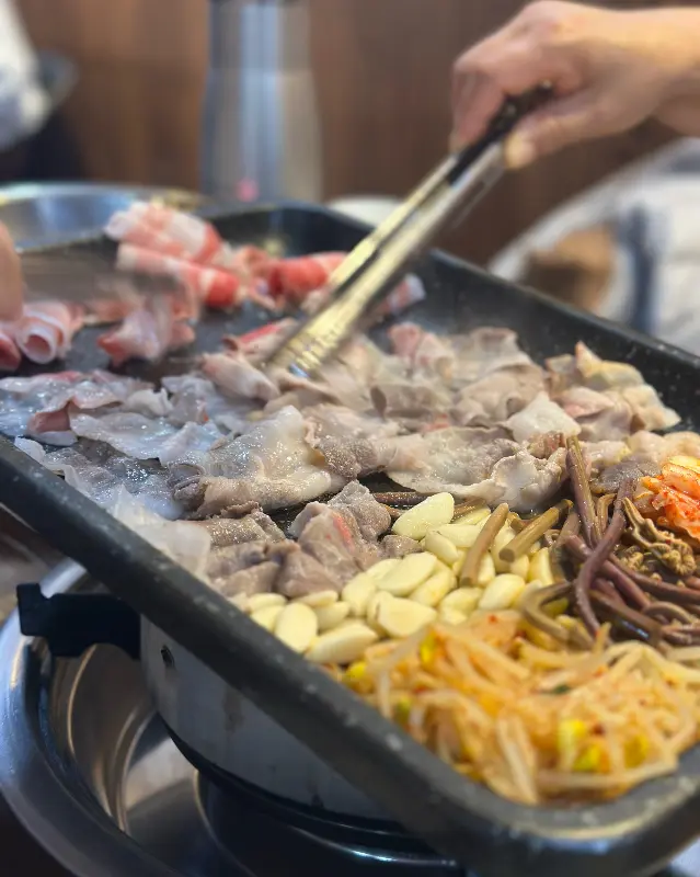 불판 위에서 익어가는 대패 삼겹살과 다채로운 곁들임 채소