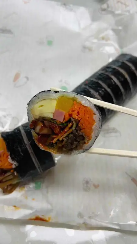 젓가락으로 집은 오징어 김밥의 단면